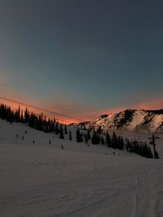 the sun is setting on a snowy mountain with people skiing down it and trees in the foreground