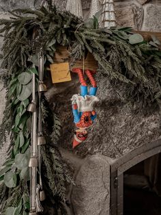 a christmas decoration hanging from the side of a stone fireplace with greenery on it