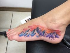 a foot with mountains painted on it and watercolors in the bottom right hand