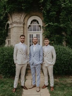 three men in suits are posing for a photo outside an old building with ivy growing around it