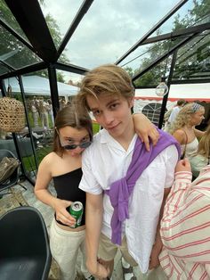 two young people standing next to each other in front of a glass tent with food and drinks