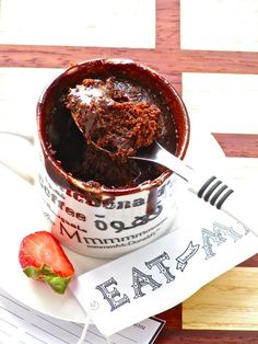 a spoonful of chocolate cake in a mug with strawberries on the side and napkins next to it