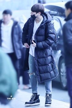 a young man is standing on the sidewalk in front of people wearing winter coats and jeans