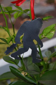 a metal ornament with a red ribbon hanging from it's side on a plant