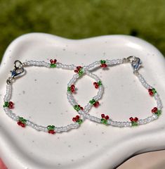 two bracelets with red, green and white beads are on a small plate in the shape of a heart