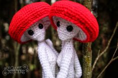 two crocheted dolls wearing red hats are sitting on a tree branch in the woods