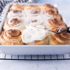 someone is cutting up some cinnamon rolls with icing on them in a baking dish