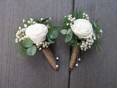 two boutonnieres with white roses and greenery are on the side of a wall