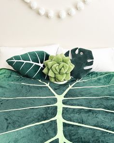 a green leaf pillow sitting on top of a bed next to a white beaded necklace