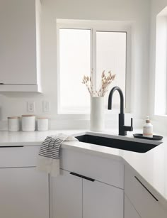 a white kitchen with black faucet, sink and countertop spacers in front of two windows