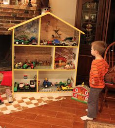 a young boy standing in front of a toy house with cars and trucks on it