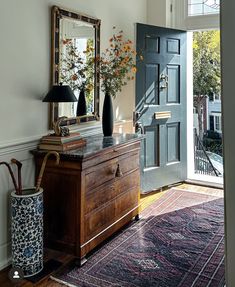 a room with a dresser, mirror and vase on the floor in front of it