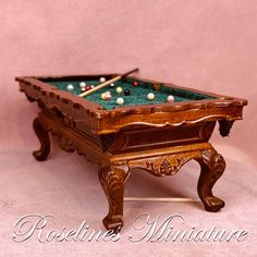 a miniature pool table with cues and balls on it's top, in front of a pink background