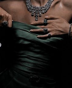 a woman in a green dress holding onto a diamond necklace and wearing an emerald ring