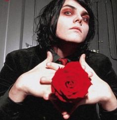 a man with black hair holding a red rose in front of his face and hands