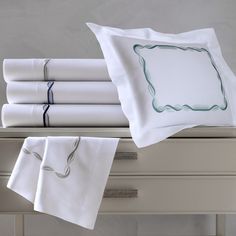 white sheets and pillow cases on a dresser with blue trim around the edges, along with an embroidered border