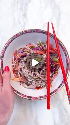 a person holding chopsticks over a bowl of food on a marble counter top