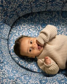 a baby laying on its back in a blue and white blanket with a sweater over it's head