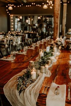 a long wooden table with candles and flowers on it, surrounded by other place settings