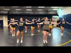 a group of young women standing on top of a gym floor holding hands in the air