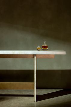 a table with a bottle and two glasses on it, sitting in front of a wall