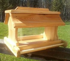 a wooden bird feeder sitting on top of a bench in the grass next to trees