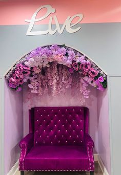 a purple couch sitting under a live flower covered arch in front of a sign that says live