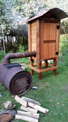 a large barrel sitting in the grass next to a firewood burning furnace and logs