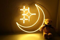 a teddy bear sitting in front of a neon sign with the moon and stars on it