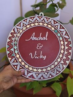 a person holding up a plate with the name and date on it in front of a potted plant