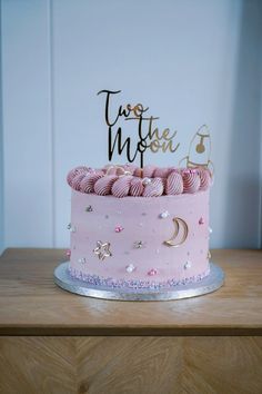 a pink and gold two tiered birthday cake with stars, moon and hearts on top