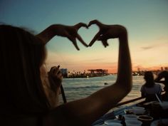 two hands making a heart shape with their fingers over the water at sunset or dawn