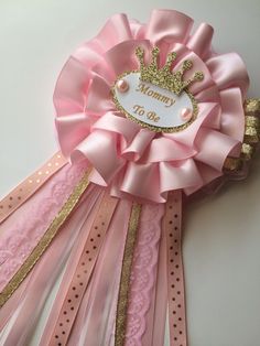 a pink ribbon with a gold crown on it that says mommy to be attached to the side