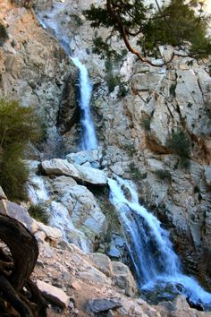 a waterfall is seen from the side of a rocky cliff, with trees and rocks in the foreground