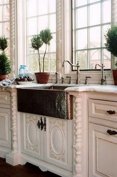 a kitchen with white cabinets and an ornate sink in the center is surrounded by potted plants