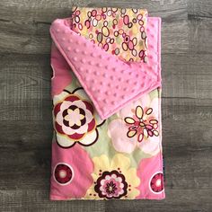 a pink and yellow flowered blanket laying on top of a wooden floor next to a pillow