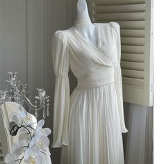 a white dress sitting on top of a mannequin next to a vase with flowers