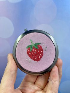 a hand holding a small embroidered strawberry