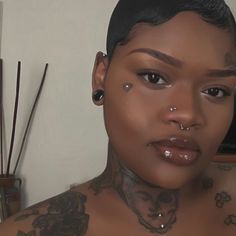 a woman with tattoos and piercings on her chest looking at the camera while standing in front of a mirror