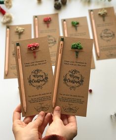 a person holding up some small cards with christmas decorations on them and pencils in front of them