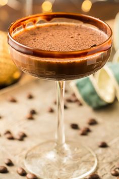 a close up of a drink in a wine glass on a table with coffee beans