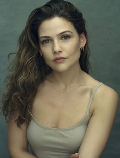 a woman with long brown hair wearing a tank top and posing for a photo in front of a gray background