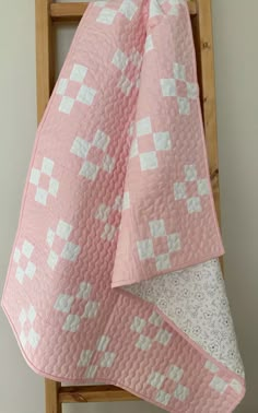 a pink and white quilted blanket sitting on top of a wooden chair