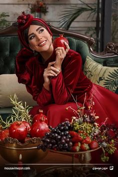 a woman in a red dress sitting on a green couch with fruit and vegetables around her