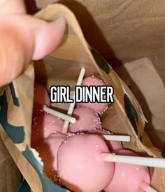 a person is holding up some pink cake pops in a paper bag with the words girl dinner on it