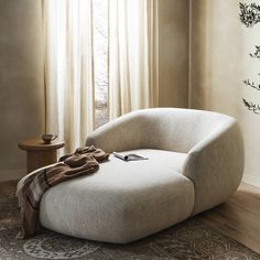 a white chair sitting on top of a wooden floor in front of a curtained window