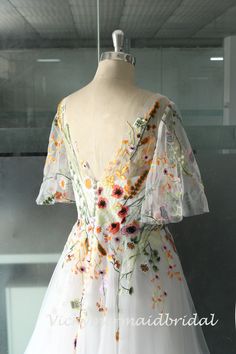 a white dress with flowers on it is displayed in a glass case at the museum