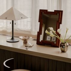 a desk with a mirror, lamp and vase on it