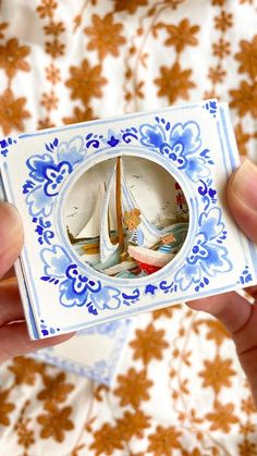 a person holding up a small blue and white plate with sailboats on it's side