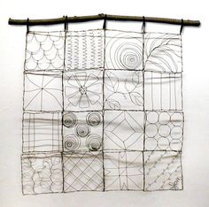 a piece of art made out of wire and paper on a white wall with a bamboo stick in front of it